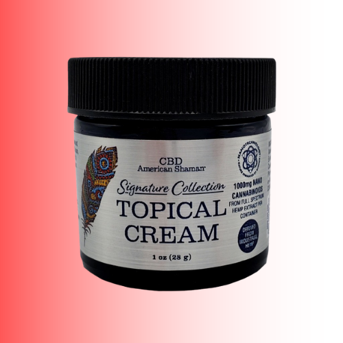 A black plastic jar of CBD American Shaman Signature Collection Topical Cream, featuring a silver label with a colorful peacock feather graphic, set against a red-to-white gradient background.